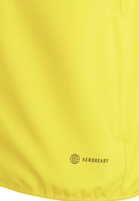 Gelbe Aeroready-Stoff mit glatter Textur. Zu den Merkmalen gehören ein Logo nahe dem Saum und eine Seitentasche. Leichtes Design für aktive Nutzung.