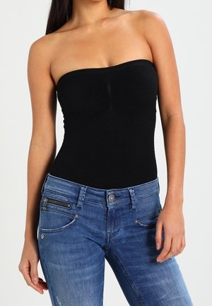 Schwarzes trägerloses Oberteil mit strukturiertem Muster, kombiniert mit blauen Denim-Jeans mit Reißverschlusstaschen und verwaschenem Look.