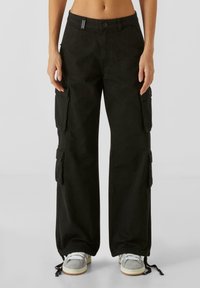 Pantalons cargo noirs en tissu robuste, dotés de jambes larges, de grandes poches latérales et de cordons de serrage ajustables aux chevilles.