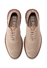 Scarpe beidge in maglia con lacci, design perforato, suola in gomma marrone contrastante e tomaia testurizzata. Nome del marchio visibile sulla soletta.