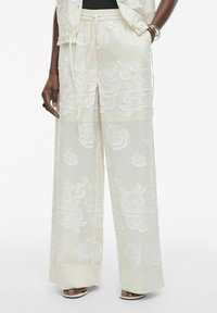 Pantalones blancos, ligeros y translúcidos con bordado floral, piernas anchas, cintura con cordón y un acabado de tela suave y texturizada.