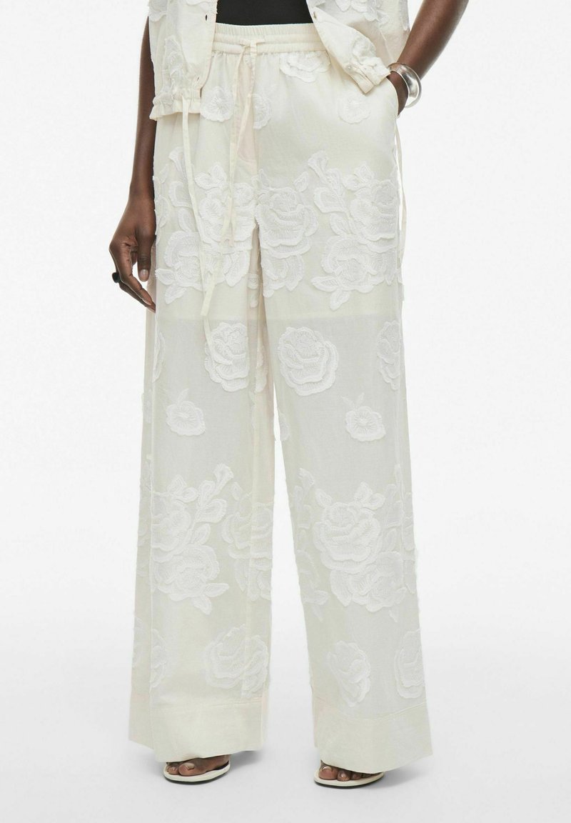 Pantalones blancos, ligeros y translúcidos con bordado floral, piernas anchas, cintura con cordón y un acabado de tela suave y texturizada.