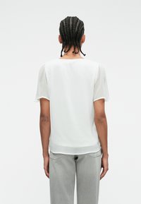 Άσπρη κοντομάνικη μπλούζα με άνετη εφαρμογή και λεία υφή, διαθέτοντας στρογγυλή λαιμόκοψη και ελαφρώς συγκεντρωμένους ώμους.