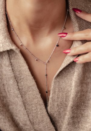 Silver chain necklace featuring small black and silver beads, with a lariat style design hanging down, worn over a beige sweater.