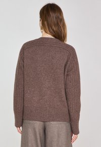 Pull en tricot marron avec texture côtelée sur les manches et l'ourlet inférieur. Coupe classique avec une silhouette légèrement décontractée, sans quincaillerie visible.