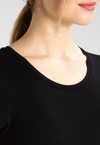 Černá bavlněná košile s kulatým výstřihem a krátkými rukávy, nabízející hladkou texturu a přiléhavý design pro elegantní vzhled.