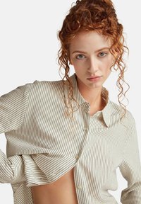 Camisa blanca con rayas verticales negras, que presenta un diseño abotonado, cuello y un corte ligeramente holgado. Tejido suave con una textura sutil.