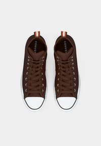Para brązowych sneakersów typu high-top Converse z białymi gumowymi noskami i paskowymi pętlami na pięcie, widziana z góry na białym tle.