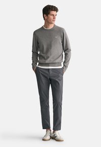 Grauer Strickpullover mit Rundhalsausschnitt, kombiniert mit dunkelgrauen Hosen und weißen Sneakers mit schwarzen Akzenten. Glatte Textur und lässige Passform.