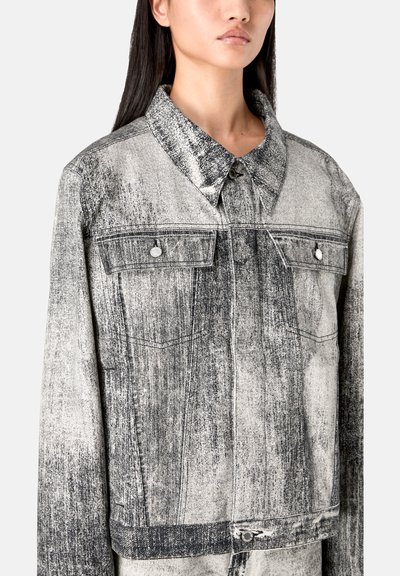 Jeansjacke mit einem schwarz-weißen beschädigten Muster, Knopfverschlüssen, umgeschlagenem Kragen und zwei Brusttaschen mit metallischen Akzenten.