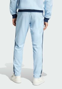 Pantaloni de trening bleu deschis, dintr-un material moale, cu dungi navy pe laterale și o croială conică, asortați cu adidași albi.