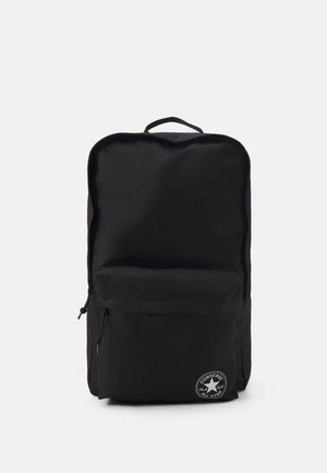 Sac à dos noir en tissu durable, avec un grand compartiment principal, une poche zippée à l'avant et un patch logo rond en bas.