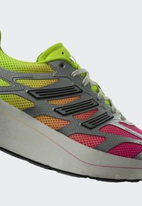 Multicolored running shoe with neon green, orange, and pink mesh upper, grey overlays, white laces, and thick white sole with red line detail.