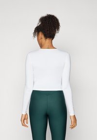 White long-sleeve top with a fitted design, paired with dark green leggings. Smooth texture with a round neckline and no visible branding.