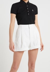 Svart pikétröja med krage och detaljer i form av knappar, i kombination med vita höga shorts med uppvikta benslut och veidig detaljer.