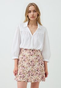 Weißes, knopf-down Hemd mit Puffärmeln; kombiniert mit einem floral gemusterten rosa Rock, der grüne und braune Akzente aufweist. Weicher, leichter Stoff.