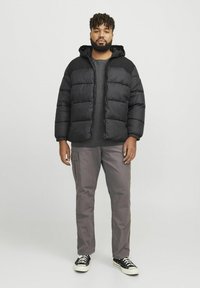 Jachetă puffer neagră cu glugă, având un design capitonat, purtată peste un pulover gri, asortată cu pantaloni cargo gri și adidași negri.