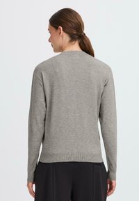 Light gray knit sweater with long sleeves, round neckline, and ribbed hem; smooth texture with a relaxed fit and side slits.
