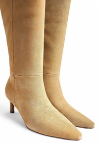 Kreemivärvi seemisnahast põlvepikkused saapad terava nina ja väikese, kitseneva kanna ülesehitusega. Siledat tekstuuri ja minimaalsete õmblusdetailidega.