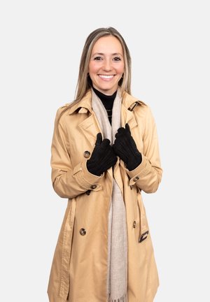 Beige trench coat over a black turtleneck, gray scarf, and black gloves. The coat features shoulder epaulets and a double-breasted front.