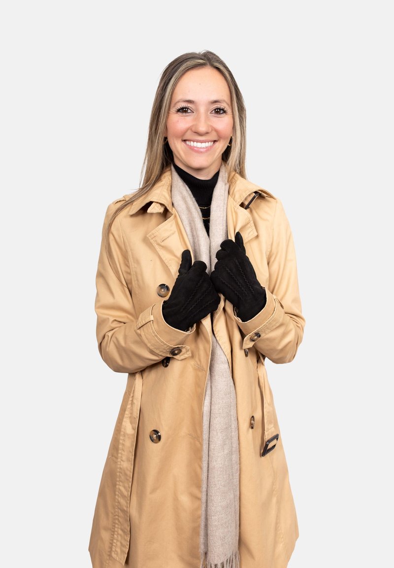 Beige trench coat over a black turtleneck, gray scarf, and black gloves. The coat features shoulder epaulets and a double-breasted front.