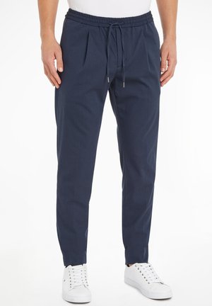 Pantaloni blu navy con vita elasticizzata e cordoncino. Presentano pieghe sul davanti e gambe affusolate. Abbinati a sneaker bianche.