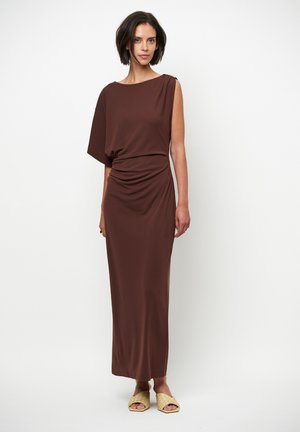 Bruine, asymmetrische maxi-jurk van gladde stof met geplooide taille. Heeft een lichte glans en een gouden accent bij de schouder.