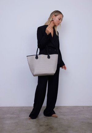 Sac fourre-tout avec une base blanche ornée d'un motif géométrique de différentes couleurs, des poignées noires et une forme structurée.
