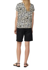 Top a maniche corte in crema con stampa animale nera, abbinato a pantaloni corti neri piegati. Il tessuto ha una texture liscia e i sandali sono piatti.