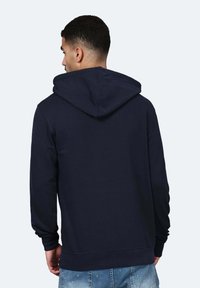 Felpa blu navy realizzata in misto cotone, con cappuccio regolabile, maniche lunghe e polsini a coste. Presenta una tasca a marsupio sul davanti.