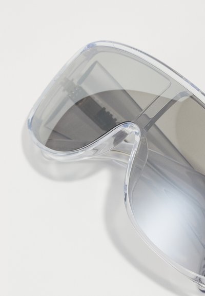 Transparent solglasögon med stora, böjda bågar, gråtonade linser och en stilren design. Har minimal hårdvara för ett strömlinjeformat utseende.
