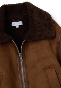 Bruine leren jas van suede met een grote bruine schapenwollen kraag, zilveren rits en details van zijzakken. De stof ziet er zacht en gestructureerd uit.