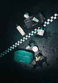 Des sacs de maquillage noirs et teal contenant divers produits de soin de la peau, y compris des crèmes et des lotions, présentés sur une surface noire texturée.