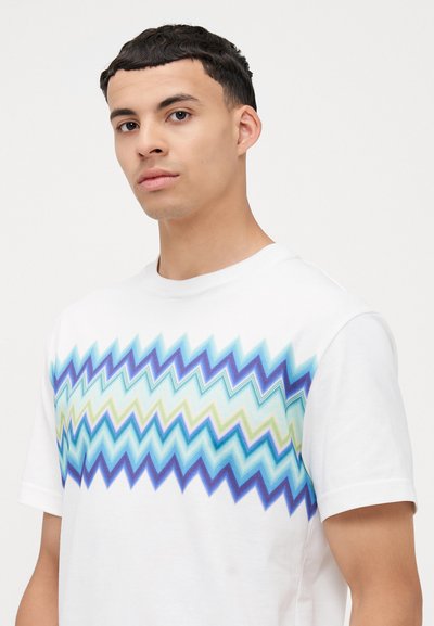 T-shirt blanc pour homme présentant un motif en zigzag dans des nuances de bleu et de vert sur la poitrine. Manches courtes, en coton, coupe décontractée.