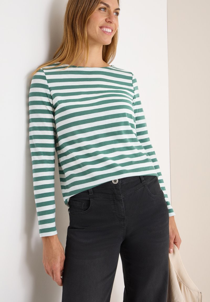 Camicia a maniche lunghe con righe orizzontali verdi e bianche, realizzata in materiale morbido. Abbinata a pantaloni neri e con una borsa di colore chiaro.