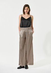 Camisola nera in satin con spalline sottili, abbinata a pantaloni larghi e patterned in beige con dettagli geometrici e vita elastica.