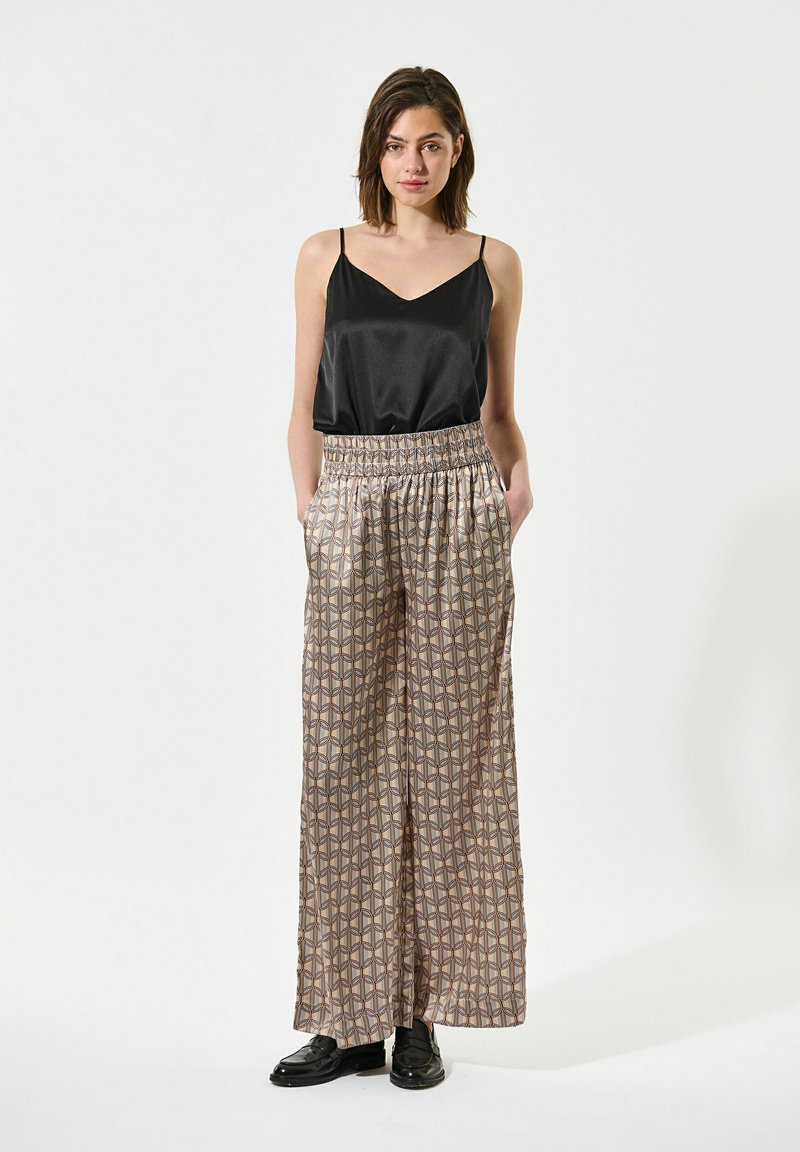 Camisola nera in satin con spalline sottili, abbinata a pantaloni larghi e patterned in beige con dettagli geometrici e vita elastica.