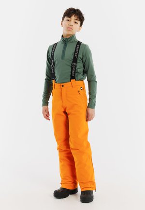 Felroze sneeuwbroeken met verstelbare zwarte bretels, gecombineerd met een groene langemouw zip-up shirt en zwarte winterlaarzen.