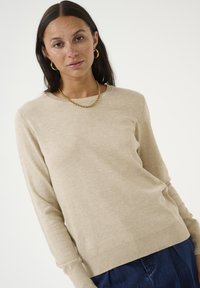 Beige crew neck sweater made of soft fabric, featuring long sleeves, ribbed cuffs and hem, paired with dark denim. Minimalistic design.
