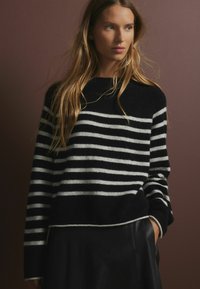 Gestreifter Pulli in Schwarz-Weiß mit Rundhalsausschnitt aus weichem Stoff, im lässigen Schnitt und mit Rippbündchen, kombiniert mit einem schwarzen Lederrock.