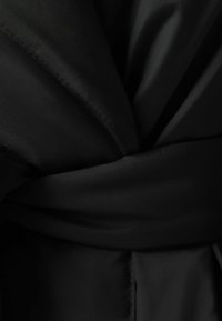 Svart bälte i tyg med en slät textur, med en bred omslagsstil och sydda detaljer längs kanterna.