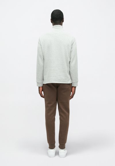 Γκρίζα φούτερ με ψηλό γιακά, χαλαρή εφαρμογή και ριγέ μανσέτες, συνδυασμένο με καφέ φόρμες και λευκά αθλητικά παπούτσια, προσανατολισμένο από πίσω.