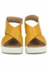 Sandali in pelle gialla con cinturini incrociati, punta aperta e suola piattaforma bianca. Presentano una soletta imbottita per il comfort.