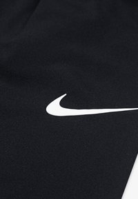 Tissu noir avec un logo Swoosh de Nike blanc. Texture lisse avec une finition légèrement mate. La vue en gros plan met en valeur le détail du logo.