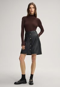Braun gestreiftes Langarmoberteil kombiniert mit einem schwarzen Leder-A-Linienrock mit goldenen Knopfakzenten und hoher Taille. Schwarze Loafers und Socken.