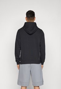 Svart hettegenser med en glatt tekstur og kengurulomme, kombinert med lysegrå shorts. Har elastiske mansjetter og søm.