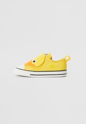 Žlutá plátěná bota s designem kachního obličeje na přední části, černobílou pruhovanou podrážkou a poutkem na zadní straně pro snadné oblékání.