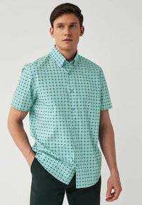 Kurzer Ärmels shirt in Hellblau mit einem geometrischen Muster aus weißen Rauten, die in Dunkelblau umrandet sind. Button-down-Kragen und glatte Stofftextur.