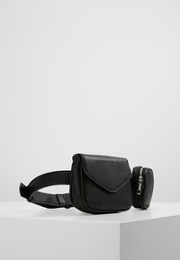 Sac banane en cuir noir avec fermeture à rabat, forme arrondie, sangle réglable et pochette amovible zippée. Texture lisse et design minimaliste.