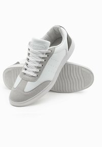 Weiße und graue Sneaker aus glattem Leder und Wildleder, mit einer strukturierten Sohle, Schnürdesign und perforierten Akzenten an den Seiten.